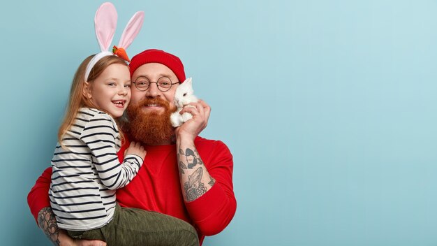 Hombre con barba pelirroja vistiendo ropas coloridas y sosteniendo a su hija