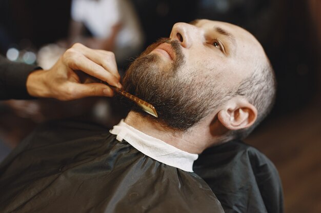 Hombre con barba. Peluquería con cliente. Hombre con peine y tijeras