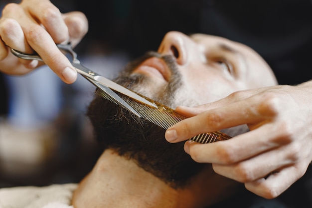 Hombre con barba. Peluquería con cliente. Hombre con peine y tijeras