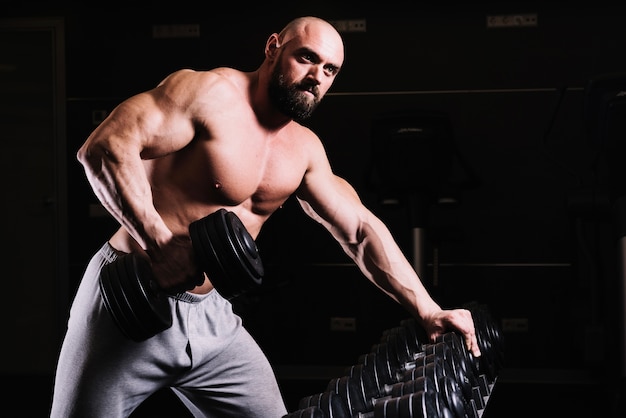 Foto gratuita hombre con barba que levanta la barra cerca de la estantería