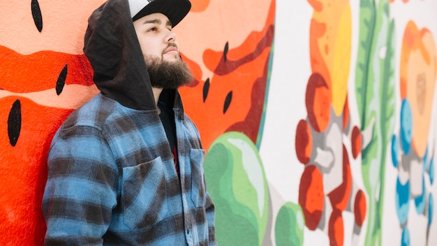 Foto gratuita hombre de la barba que está parado delante de la pared colorida del graffiti