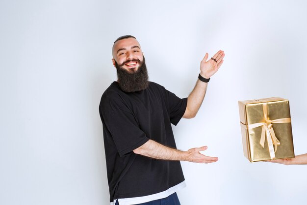 Hombre con barba recibiendo una caja de regalo de color dorado.