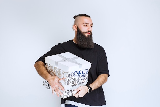 Hombre con barba sosteniendo una caja de regalo azul blanca y parece decepcionado.