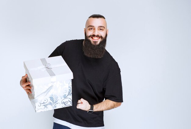Hombre con barba sosteniendo una caja de regalo azul blanca y sintiéndose exitoso.