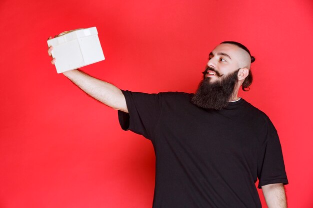 Hombre con barba sosteniendo una caja de regalo blanca con satisfacción.