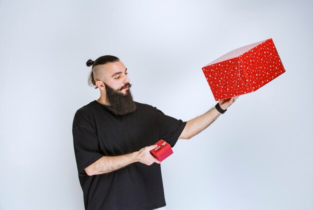 Hombre con barba sosteniendo cajas de regalo rojas en ambas manos y tomando una decisión.