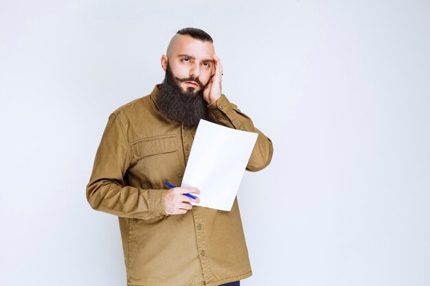 Hombre con barba sosteniendo un cuestionario y parece confundido y pensativo.