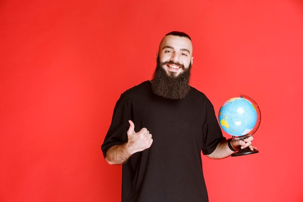 Hombre con barba sosteniendo un globo terráqueo y apuntando a algún lugar.