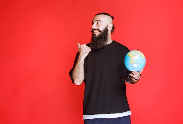 Hombre con barba sosteniendo un globo terráqueo y apuntando a algún lugar.