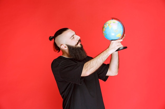 Hombre con barba sosteniendo un globo terráqueo y buscando lugares sobre él.