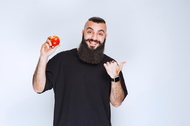 Hombre con barba sosteniendo una manzana roja o melocotón y disfrutando del sabor.