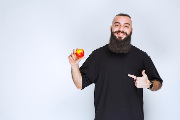 Hombre con barba sosteniendo una manzana roja o melocotón.