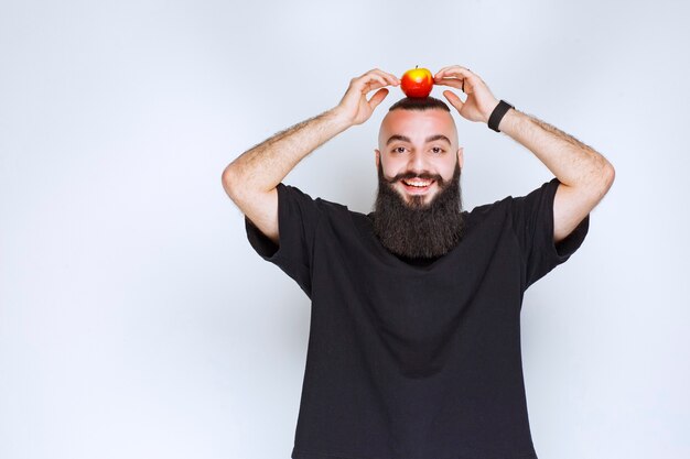 Hombre con barba sosteniendo manzanas sobre su cabeza.