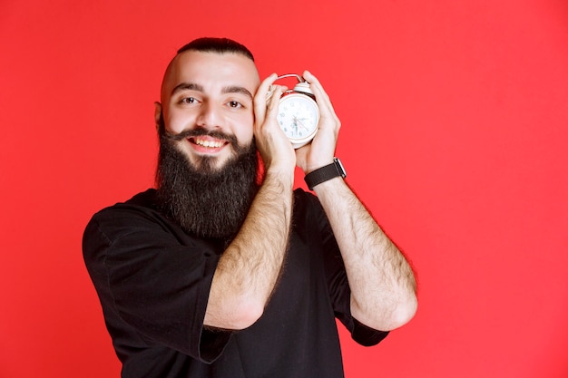Hombre con barba sosteniendo y promocionando un despertador como producto.