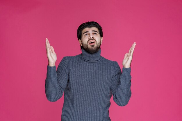 Hombre con barba sosteniendo sus manos de una manera como si estuviera rezando o deseando algo.