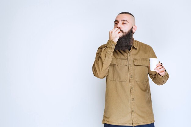 Hombre con barba sosteniendo una taza de café y disfrutando del sabor.