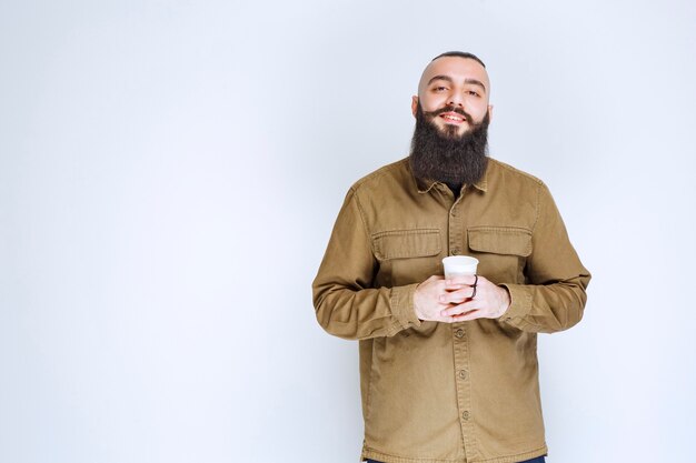 Hombre con barba sosteniendo una taza de café en una taza desechable.