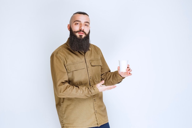 Hombre con barba sosteniendo una taza de café en una taza desechable.