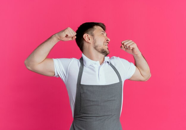 Hombre barbero en delantal estirándose sintiendo fatiga matutina de pie sobre fondo rosa