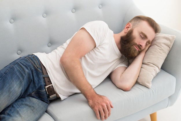 Hombre barbudo acostado y dosificación en sofá
