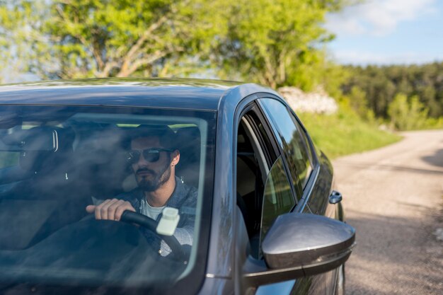 Hombre barbudo adulto conduciendo un coche en un día soleado