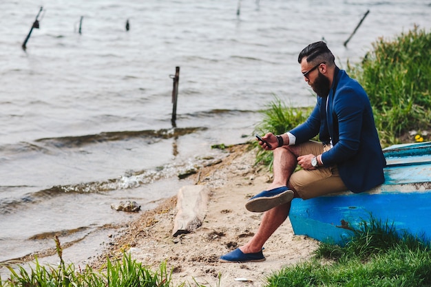 Hombre barbudo americano mira a la orilla del río con una chaqueta azul