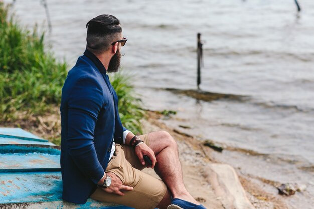 Hombre barbudo americano mira a la orilla del río con una chaqueta azul