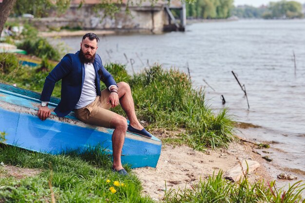 Hombre barbudo americano mira a la orilla del río con una chaqueta azul