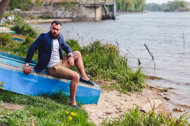 Hombre barbudo americano mira a la orilla del río con una chaqueta azul