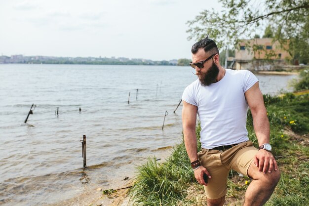 Hombre barbudo americano mira a la orilla del río con una chaqueta azul