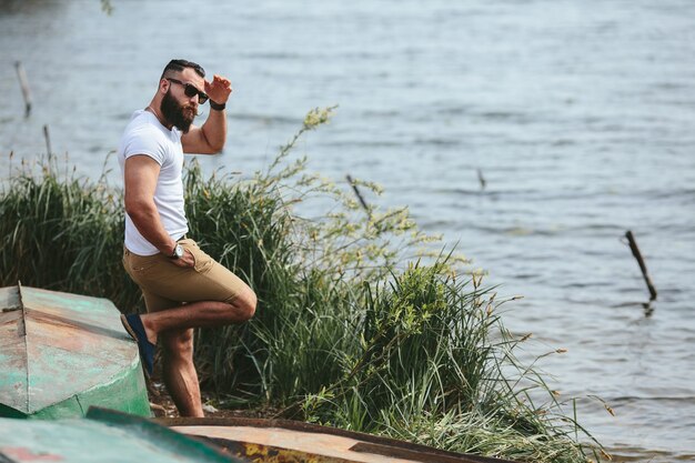 Hombre barbudo americano mira a la orilla del río con una chaqueta azul