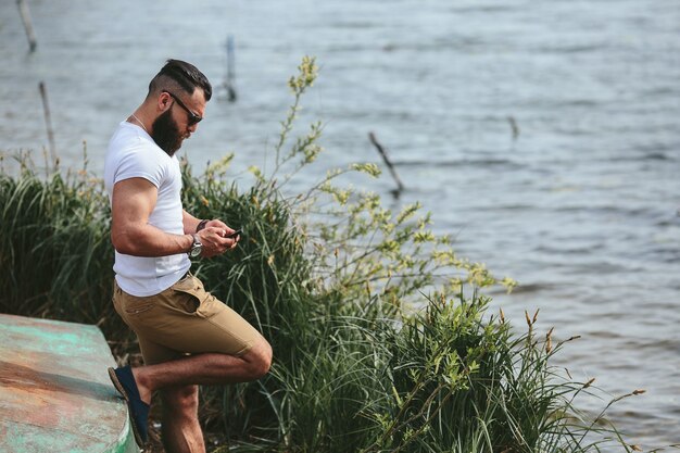 Hombre barbudo americano mira a la orilla del río con una chaqueta azul