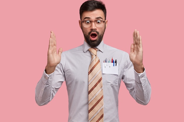 El hombre barbudo asombrado y sorprendido gesticula activamente, muestra algo muy grande, tiene expresión de sorpresa, usa camisa formal con corbata