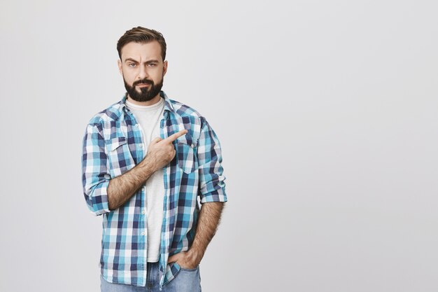 Hombre barbudo de aspecto serio escéptico apuntando hacia la esquina superior derecha