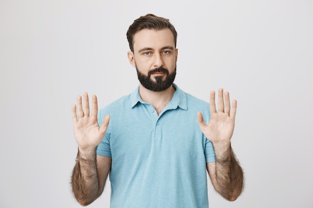 Hombre barbudo de aspecto serio mostrando gesto de parada, manos vacías