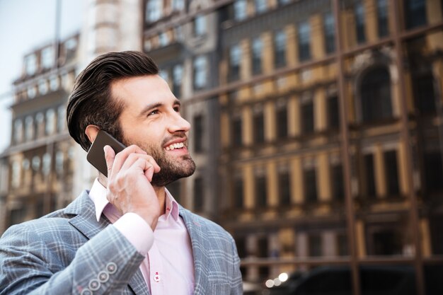 Hombre barbudo atractivo en chaqueta hablando por teléfono móvil