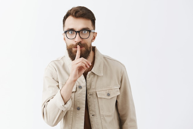 Hombre barbudo con barba emocionado en gafas posando contra la pared blanca