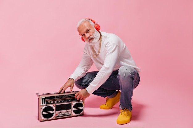 Hombre barbudo blanco con suéter blanco escuchando música con auriculares naranjas y encendiendo un tocadiscos en un fondo aislado