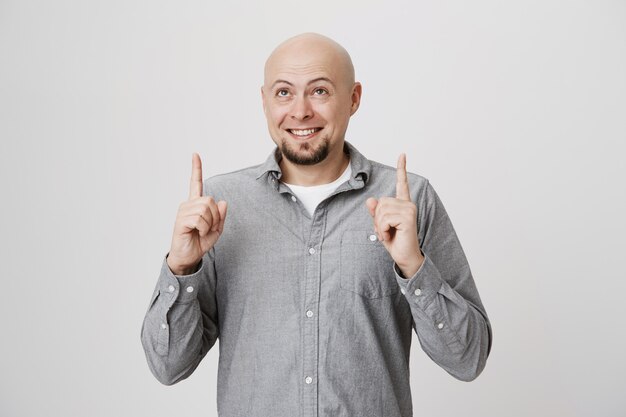 Hombre barbudo Calvo sonriente apuntando y mirando hacia arriba