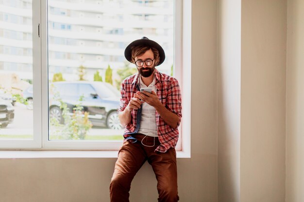 Hombre barbudo en camisa a cuadros brillante instalar nueva aplicación móvil en dispositivo de teléfono inteligente y escuchar música. Estilo hipster.