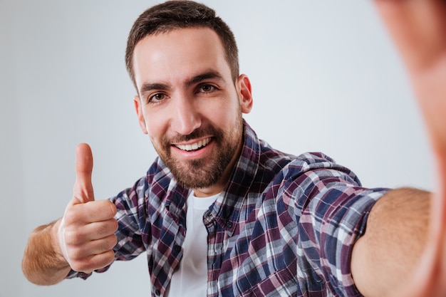 Foto gratuita hombre barbudo en camisa haciendo selfie y mostrando el pulgar hacia arriba