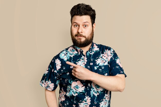 Hombre barbudo en camisa de verano floral apuntando hacia el lado