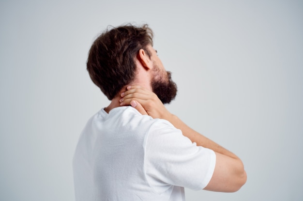 Hombre barbudo en una camiseta blanca medicina para el estrés dolor en el cuello fondo claro