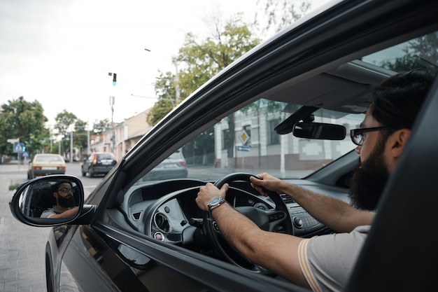 Hombre barbudo casual moderno conduciendo un automóvil