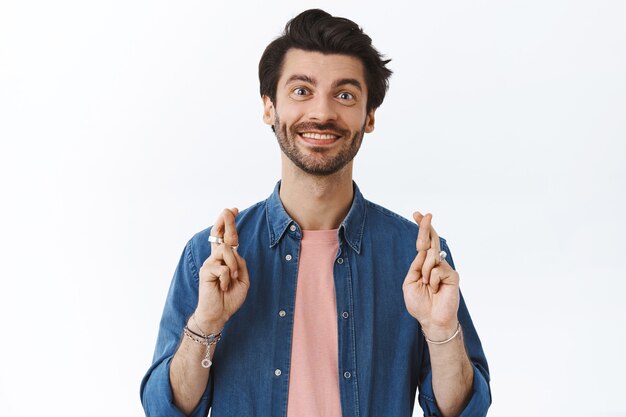 Hombre barbudo caucásico alegre cree que los sueños se hacen realidad, anticipando una gran fortuna, sonriendo con alegría, ganando recibir algo bueno, pared blanca