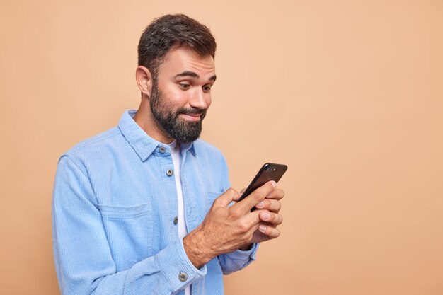 Hombre barbudo complacido sonríe alegremente mientras lee el mensaje recibido en el teléfono inteligente