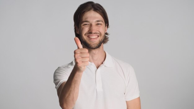 Hombre barbudo confiado manteniendo el pulgar hacia arriba luciendo feliz sobre fondo blanco Chico atractivo sonriendo a la cámara mostrando el signo aprobado aislado