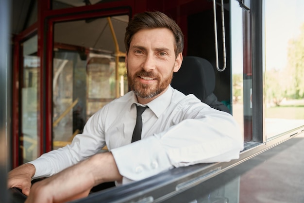 Foto gratuita hombre barbudo confiado sentado en el asiento del conductor con un brazo apoyado en el retrato de la ventana abierta