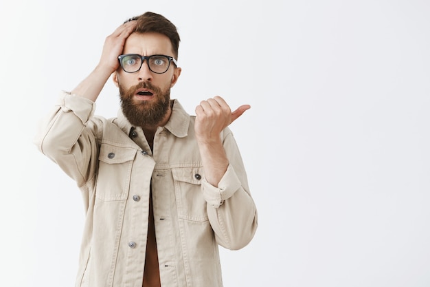 Foto gratuita hombre barbudo confundido y preocupado con gafas posando contra la pared blanca