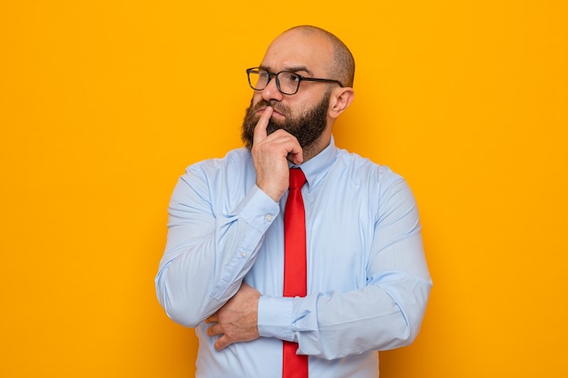 Hombre barbudo con corbata roja y camisa azul con gafas mirando a un lado desconcertado